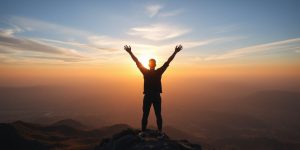 Person on mountain peak at sunrise, arms raised.